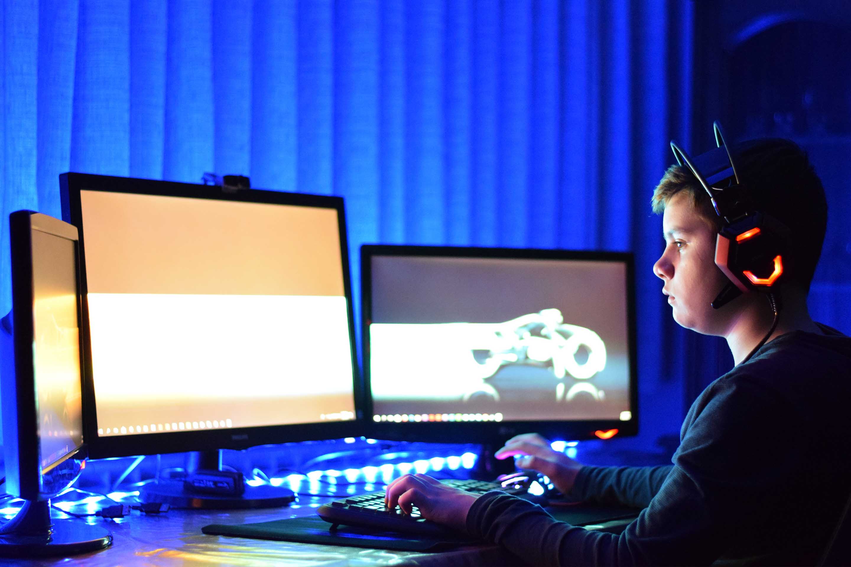 niño con auriculares frente a tres monitores con fondo azul