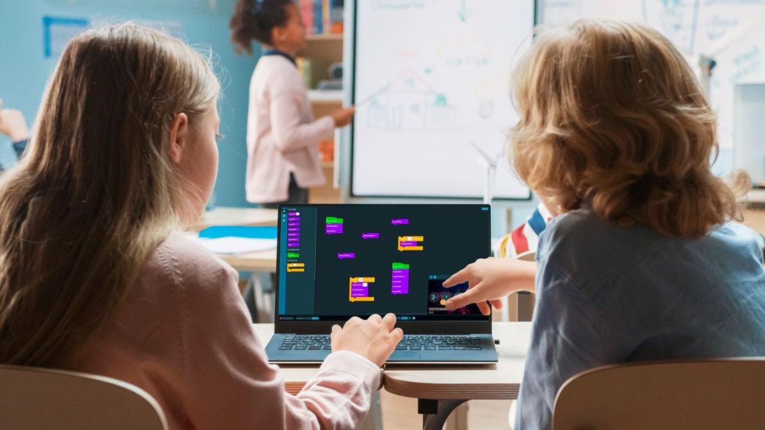 a girl and a boy sitting next to each other looking at a laptop with programming on the screen