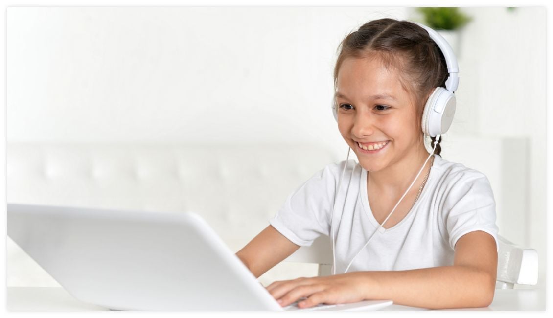 lächelndes Mädchen im weißen T-Shirt mit Kopfhörer vor dem Laptop