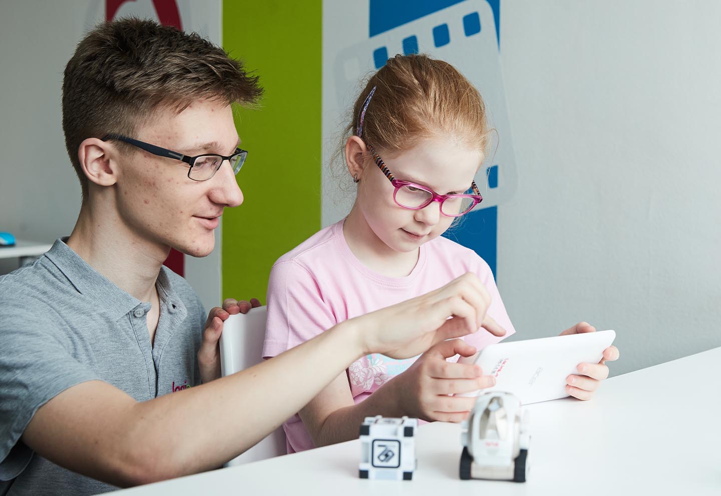 Kleines Mädchen in rosafarbenem T-Shirt und Brille mit einem Trainer in grauem T-Shirt, der auf ein Tablet schaut