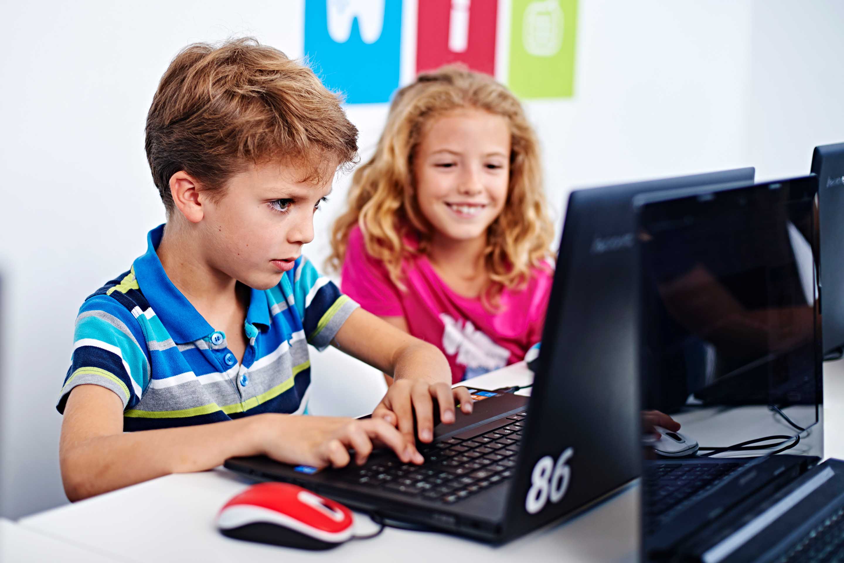 boy in striped t-shirt next to girl in pink t-shirt in front of a computer coding