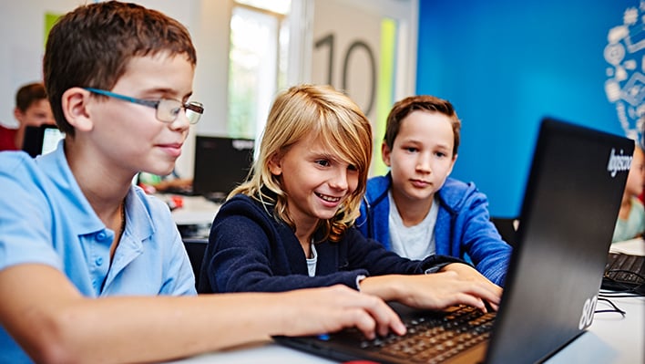 Drei Jungen in blauen T-Shirts vor einem Laptop