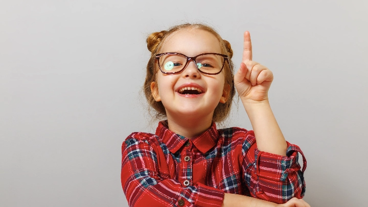 little girl in red shirt pointing up in front of white background